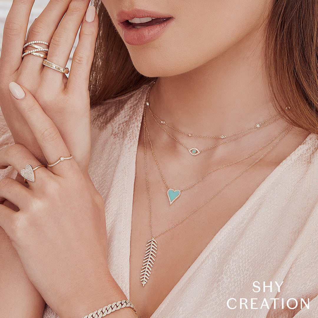 Close-up of a woman wearing gold necklaces, rings, and a bracelet with 'SHY CREATION' branding.