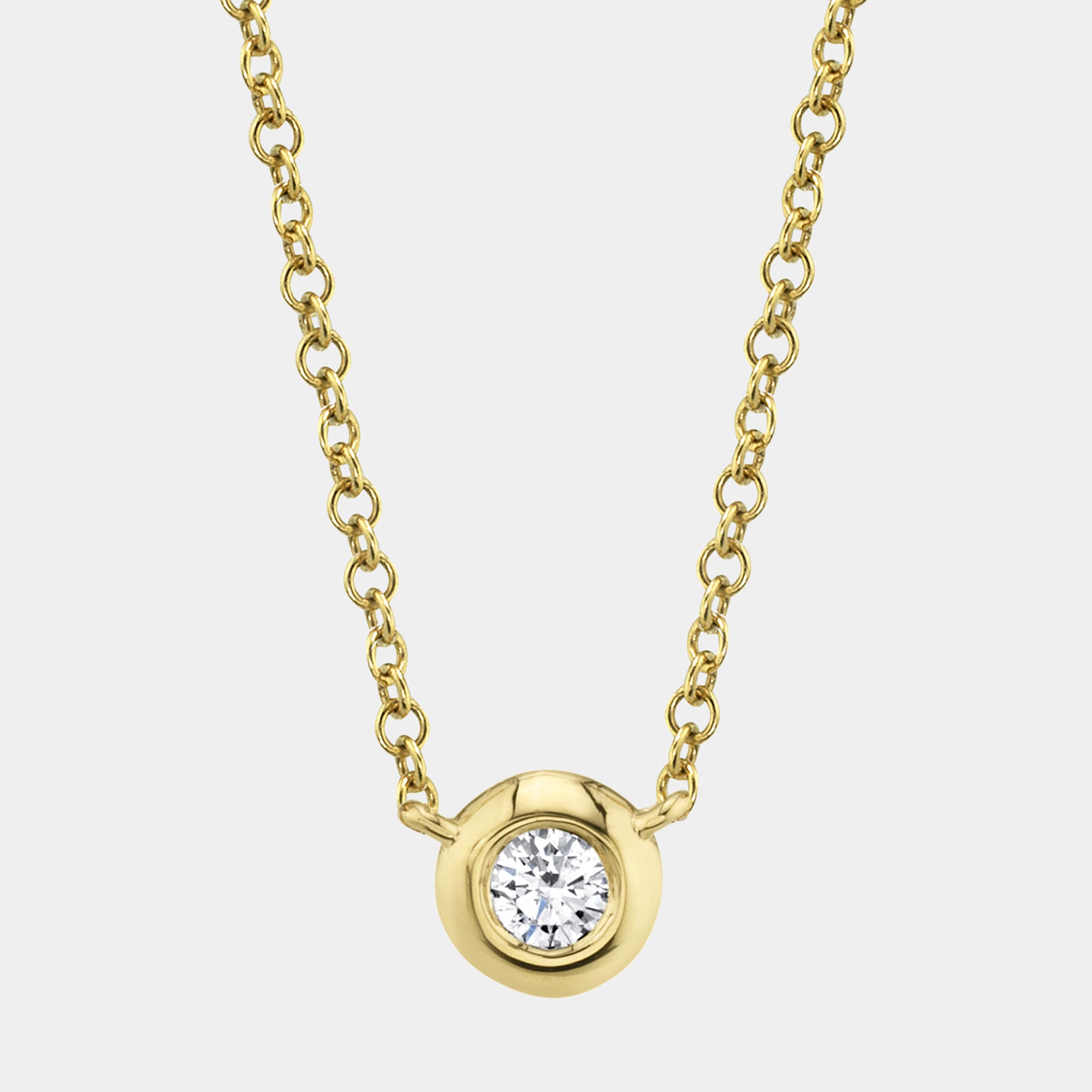 Gold necklace with a diamond bezel  pendant on a light gray background