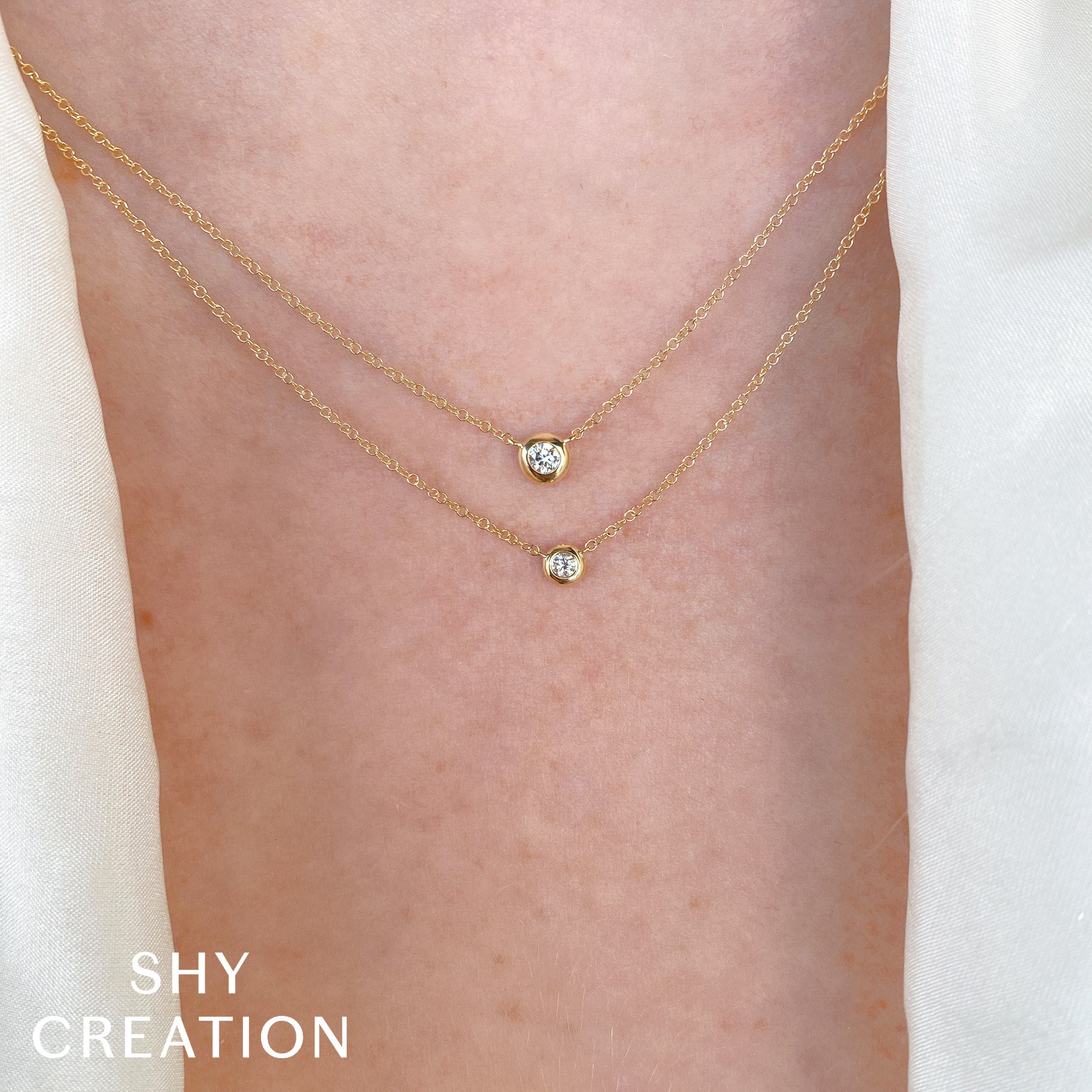 Gold bezel necklace with small diamonds on a person's neck, branded 'SHY CREATION'.