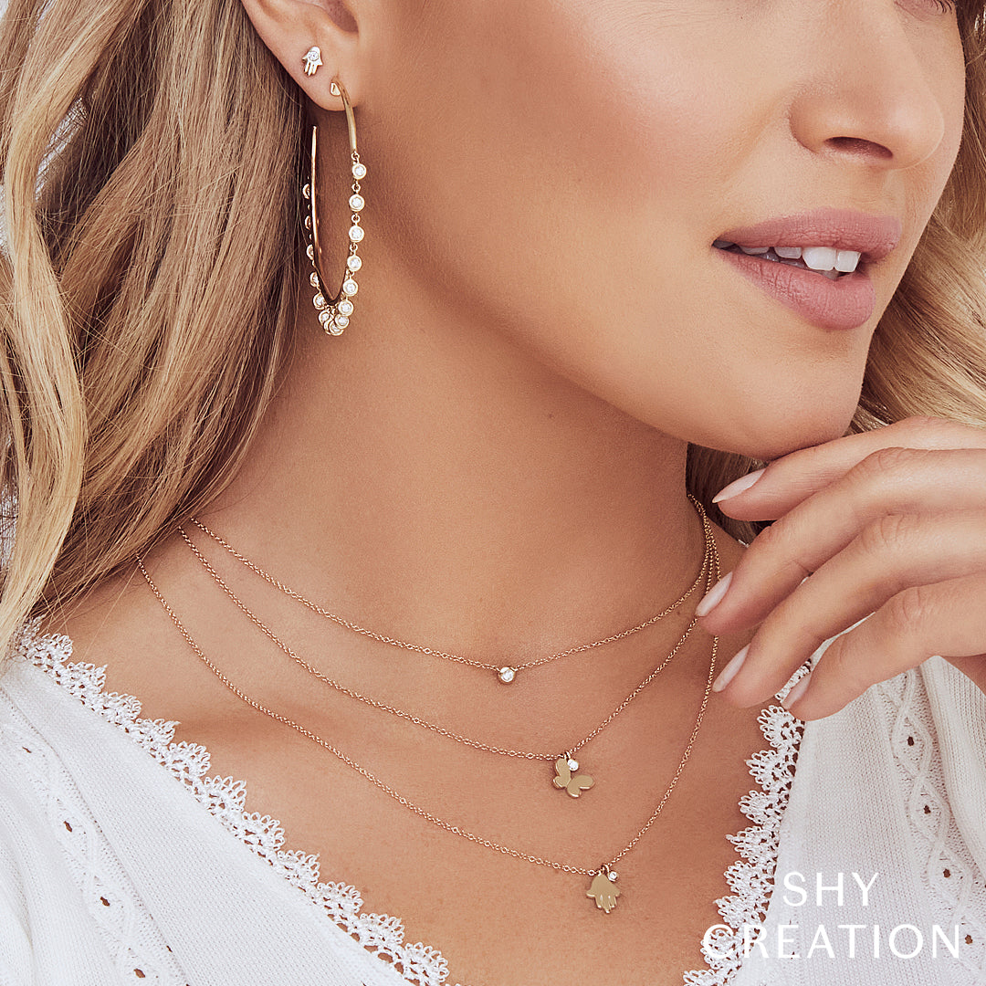 Close-up of a woman wearing gold necklaces and earrings with 'SHY CREATION' branding.