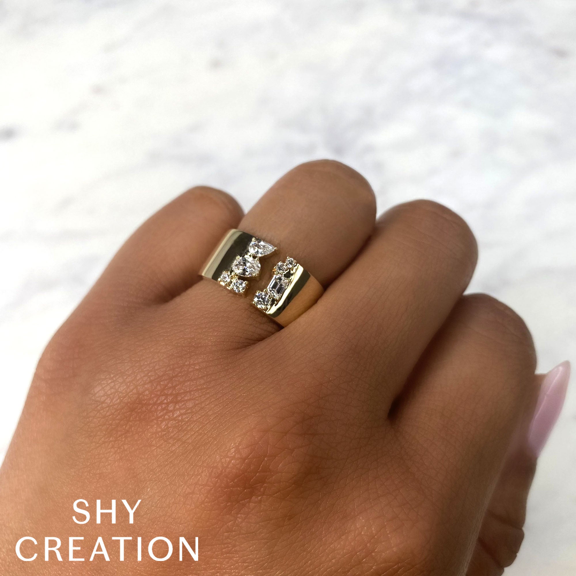 Woman's hand wearing yellow gold emerald pear and oval shaped diamond cocktail ring