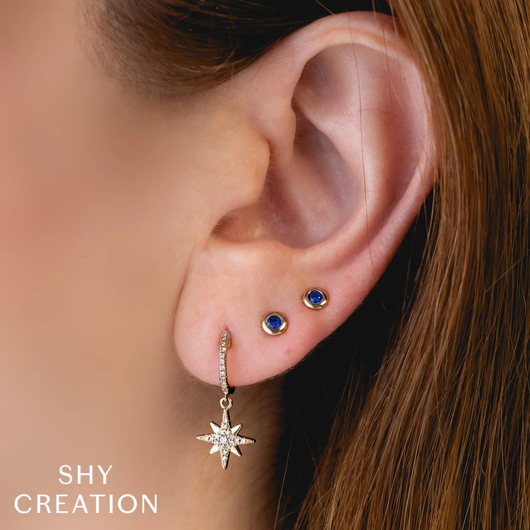 Close up of woman wearing white gold bezel set sapphire stud earrings, front angle view