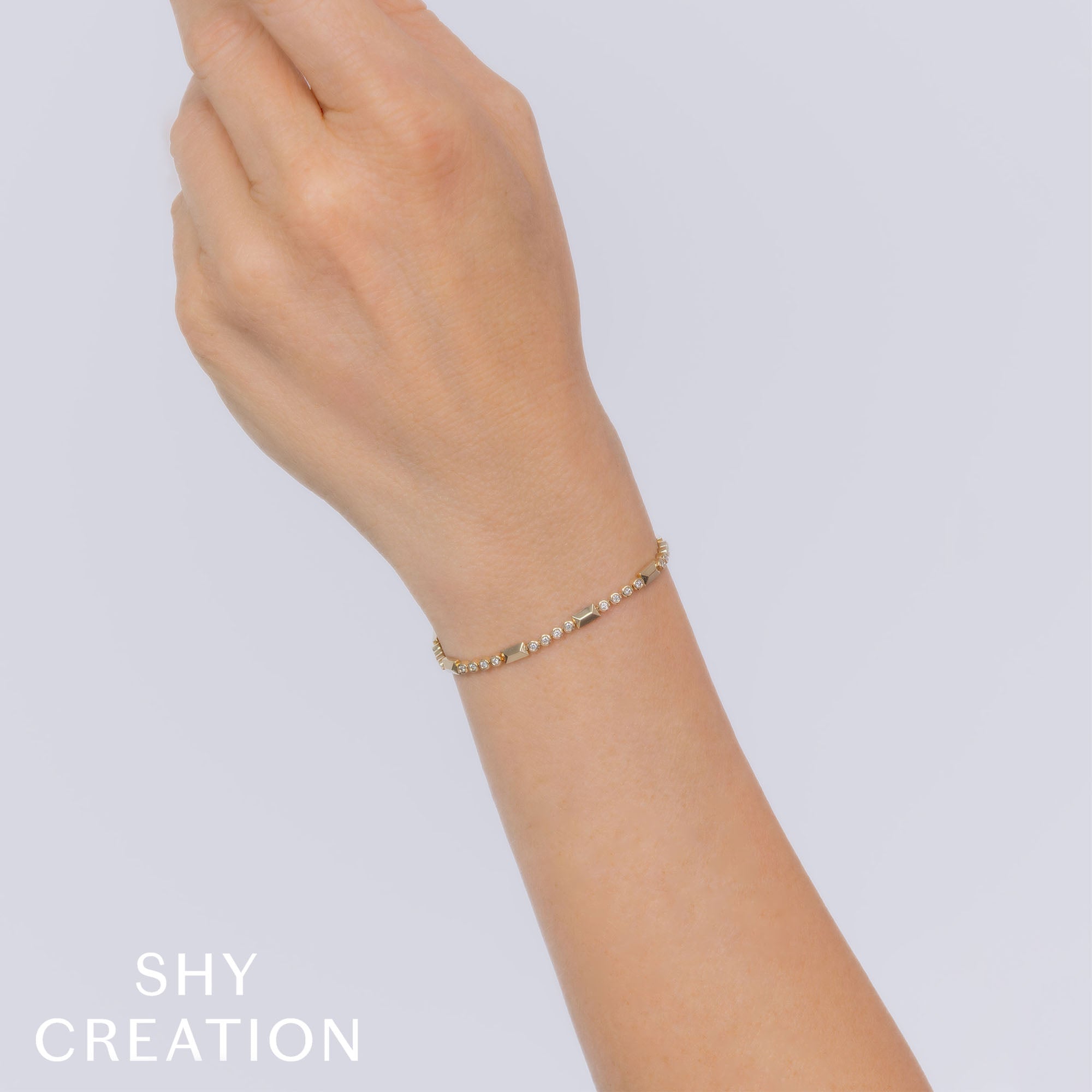 Woman wearing yellow gold geo cut diamond tennis bracelet, wrist closeup