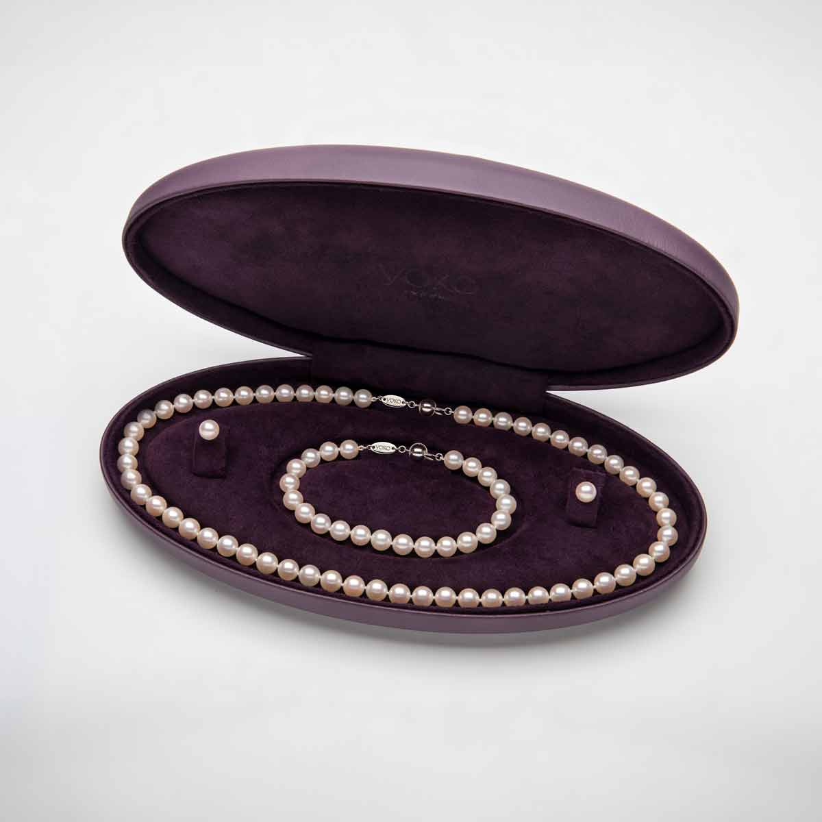 Pearl jewelry set including necklace, bracelet, and earrings in an open purple jewelry box on a white background.