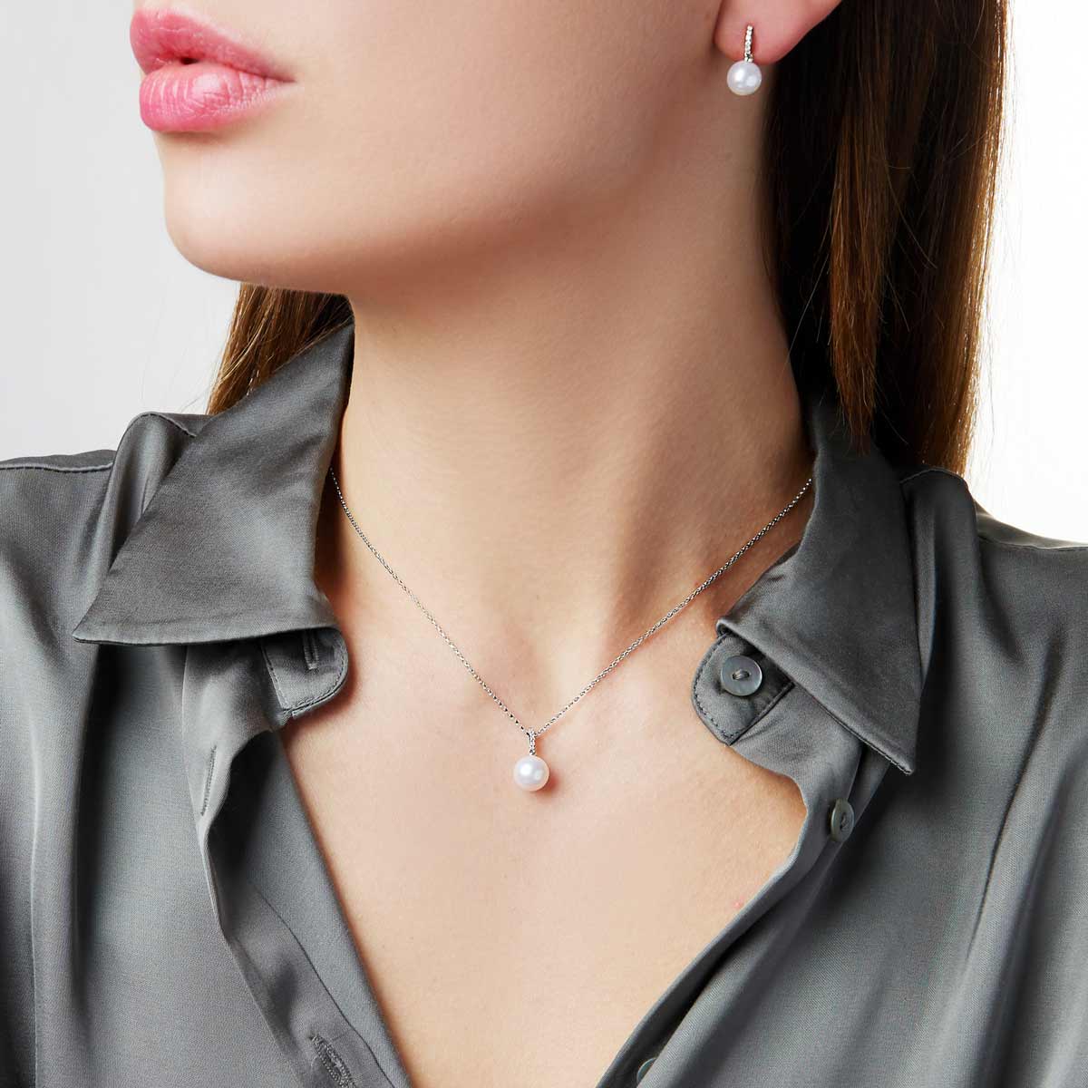 Pearl necklace and earrings on a person wearing a gray shirt.