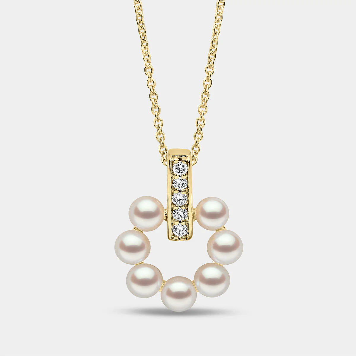 Yellow gold pearl pendant with diamond accents on grey background, front view