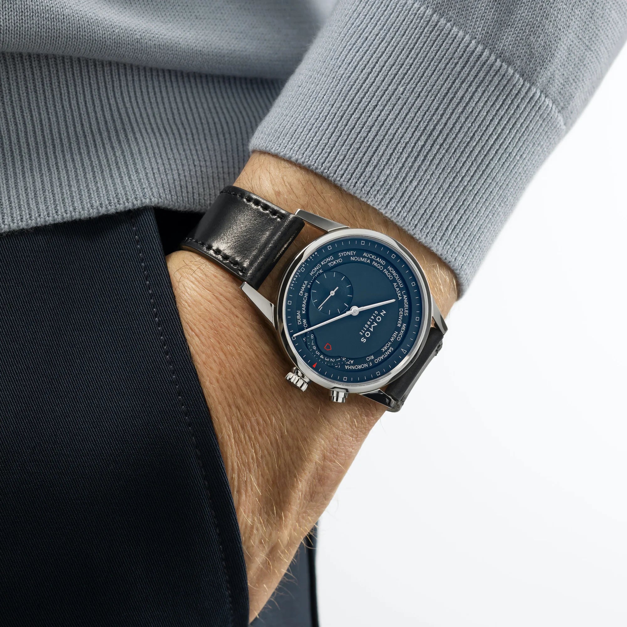 Wrist wearing a NOMOS watch with a blue face and black strap, against a neutral background.