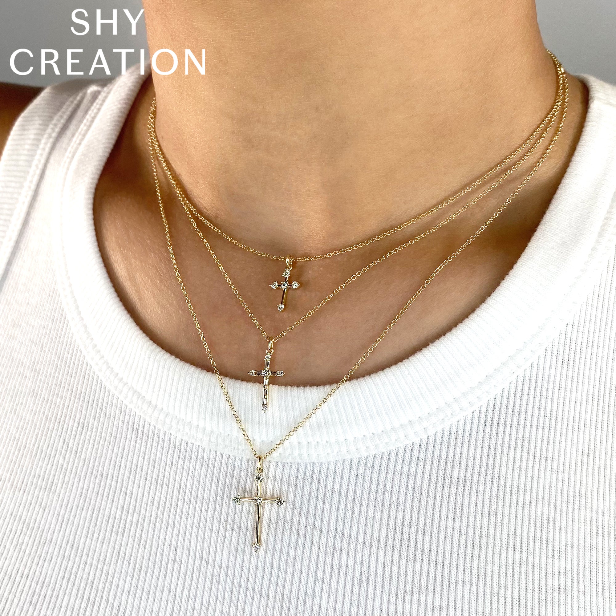 Close-up of a person wearing multiple gold necklaces with cross pendants on a plain background.